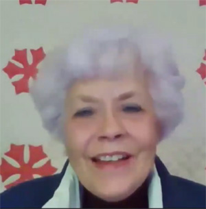 Pamela Cory is a white woman with white hair that curls softly around her face, and is smiling as she speaks.